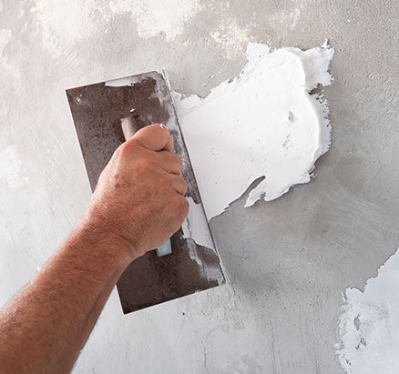 Hand applying patching compound to a stucco wall with a trowel