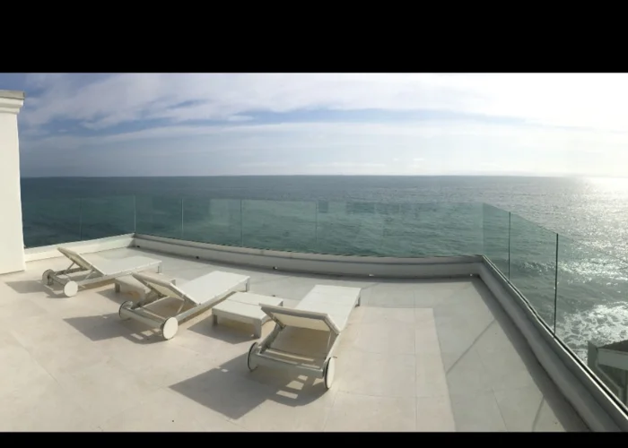 Ocean-view roof deck with a white railing and sun loungers