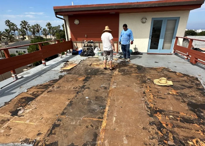 Two workers applying a waterproof coating to a roof deck