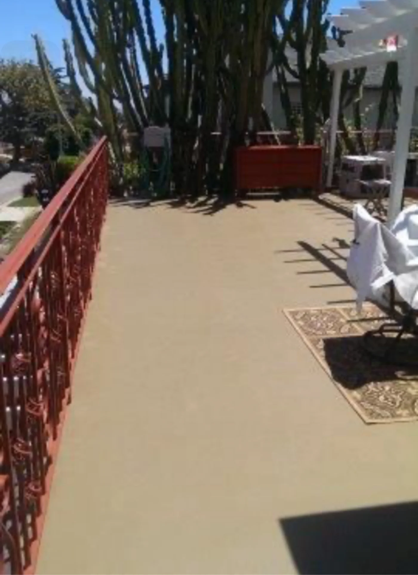 Tan-coated deck walkway with a red metal railing on a hillside property